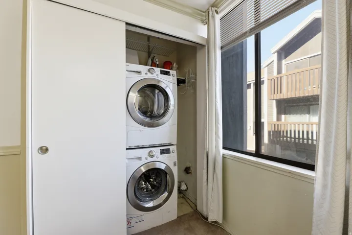 Integrated laundry closet with stacked washer and dryer, featuring white sliding doors and an upper wire shelf