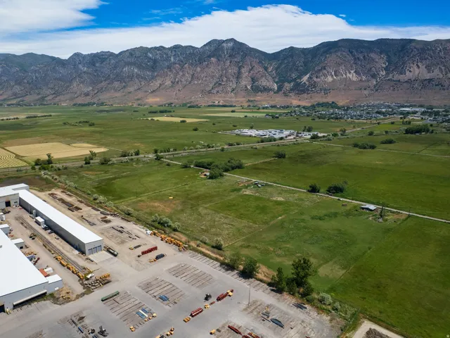 Expansive mountain range backdrop framing agricultural fields and a developed commercial property with multiple large warehouse structures, extensive paved parking, and visible storage areas