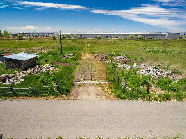 Expansive green field featuring a gravel access path, a metal gate, and a rustic wooden shed