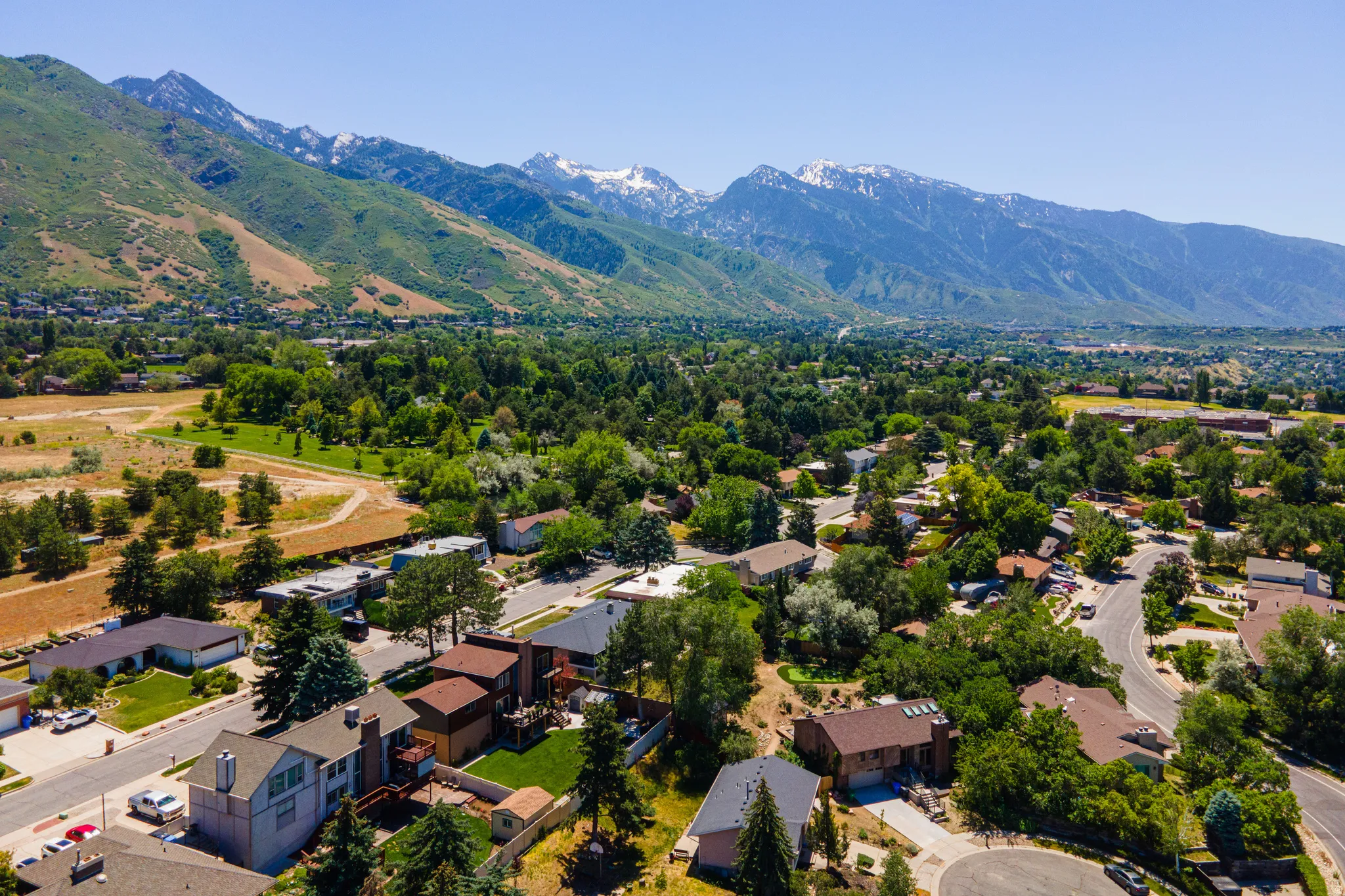 Expansive mountain range backdrop framing a residential neighborhood with mature trees, green spaces, and curving streets