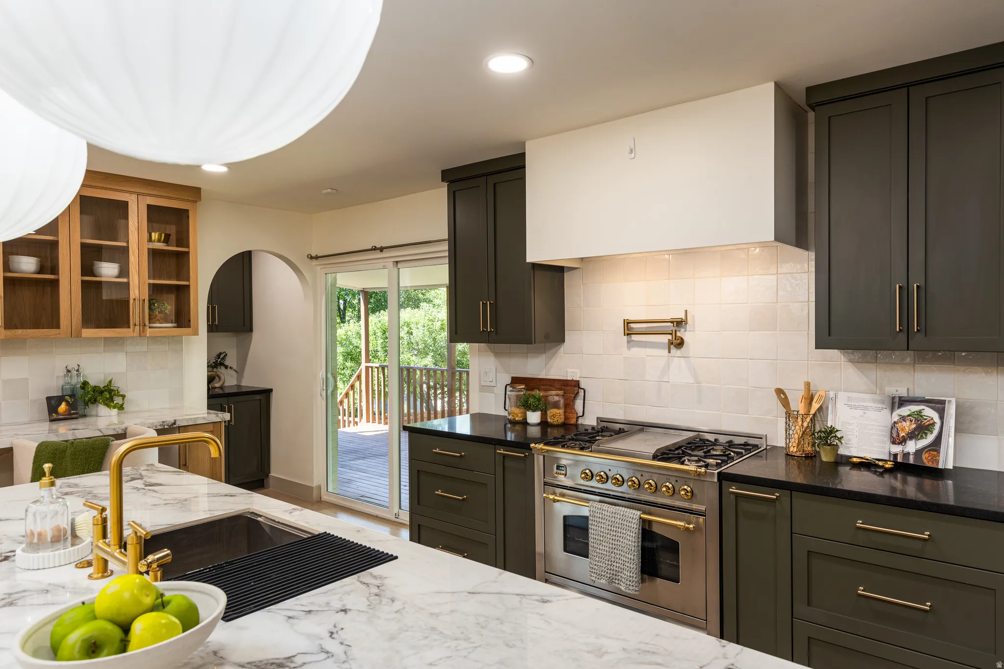 Kitchen featuring dark cabinetry, lighter wood-finish upper cabinets with glass panels, and a white marble-patterned countertop with an undermount sink