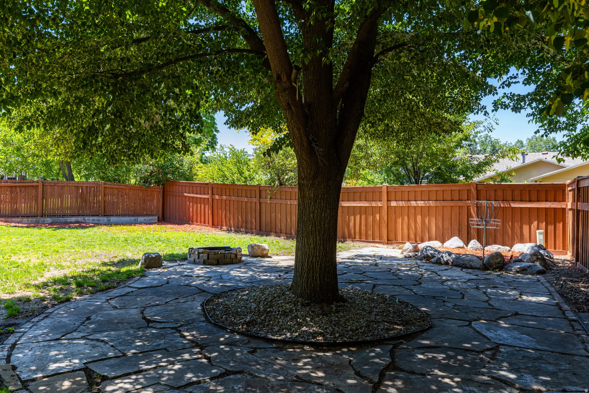 Private backyard featuring a stone patio, mature shade tree, and a built-in fire pit