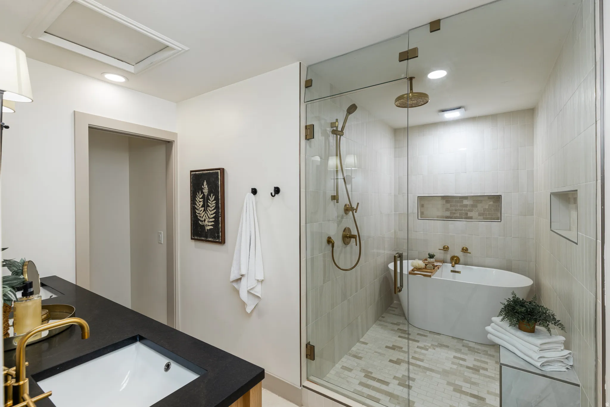 Spacious bathroom featuring a frameless glass shower enclosure, a freestanding oval soaking tub with brass fixtures, and a vanity with a dark countertop and undermount sink