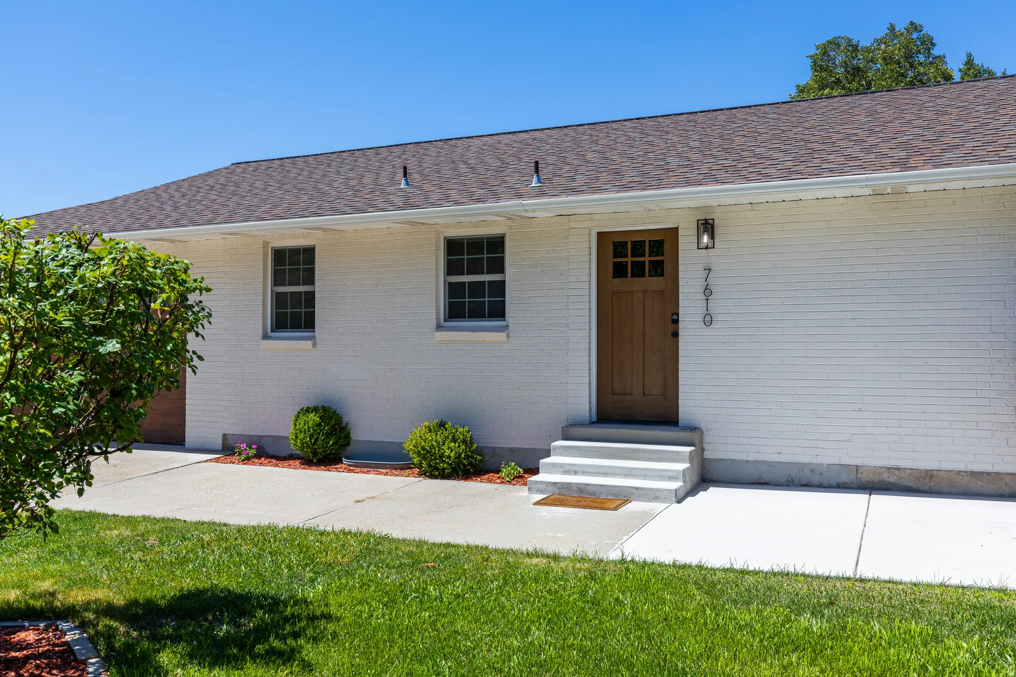 White brick exterior with a wood-finish front door, accented by a contemporary exterior light fixture and house numbers