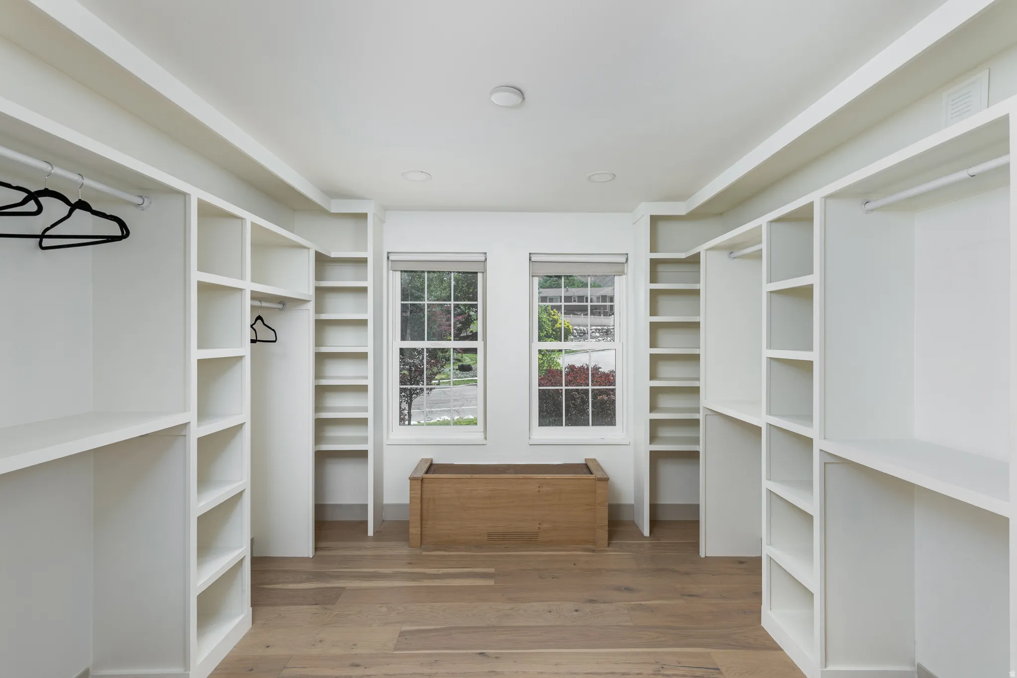 Expansive closet featuring wood-finish flooring, two large windows, white built-in shelving, and integrated hanging rods