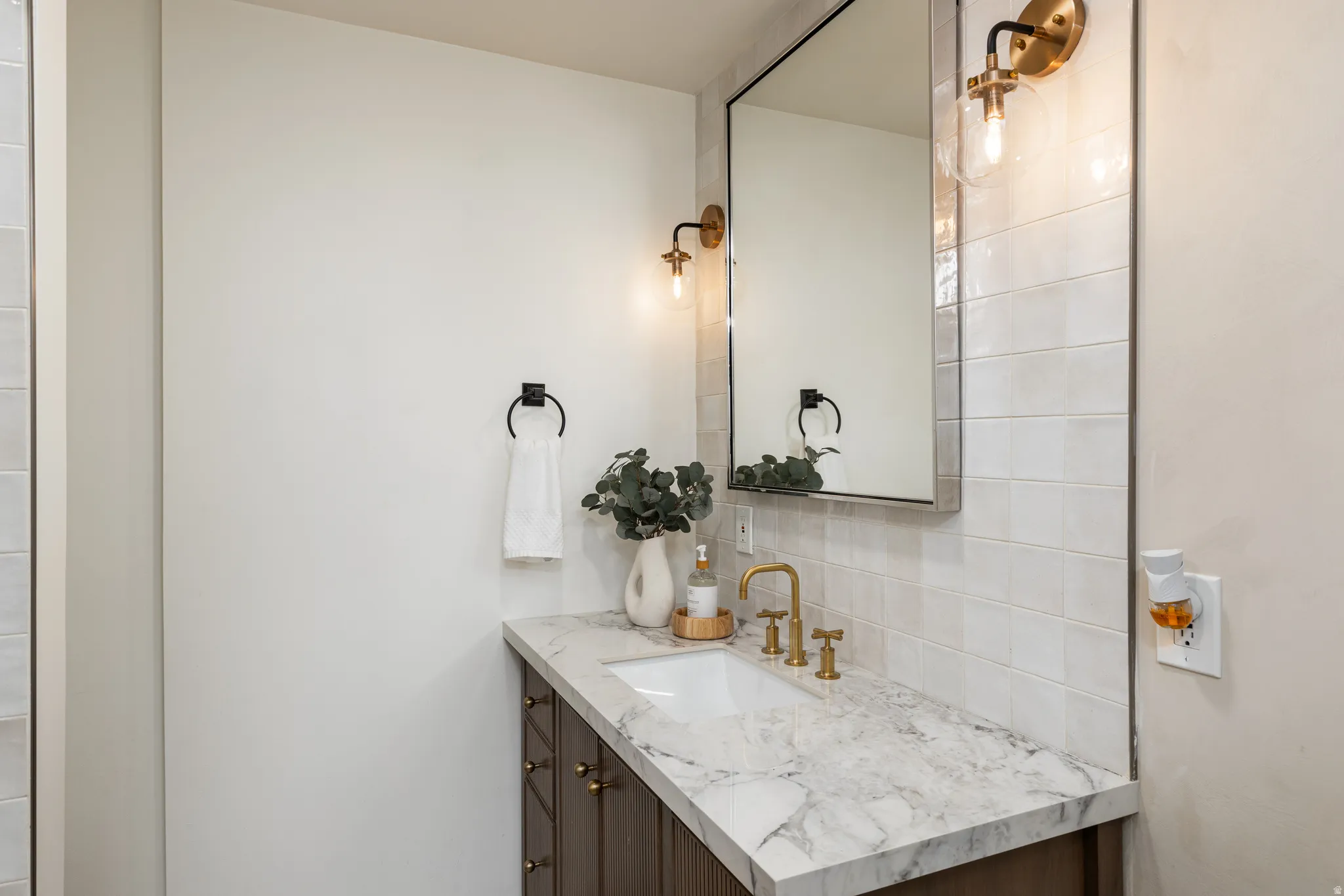 Bathroom vanity featuring a natural stone countertop with an undermount sink and brass-finish faucet