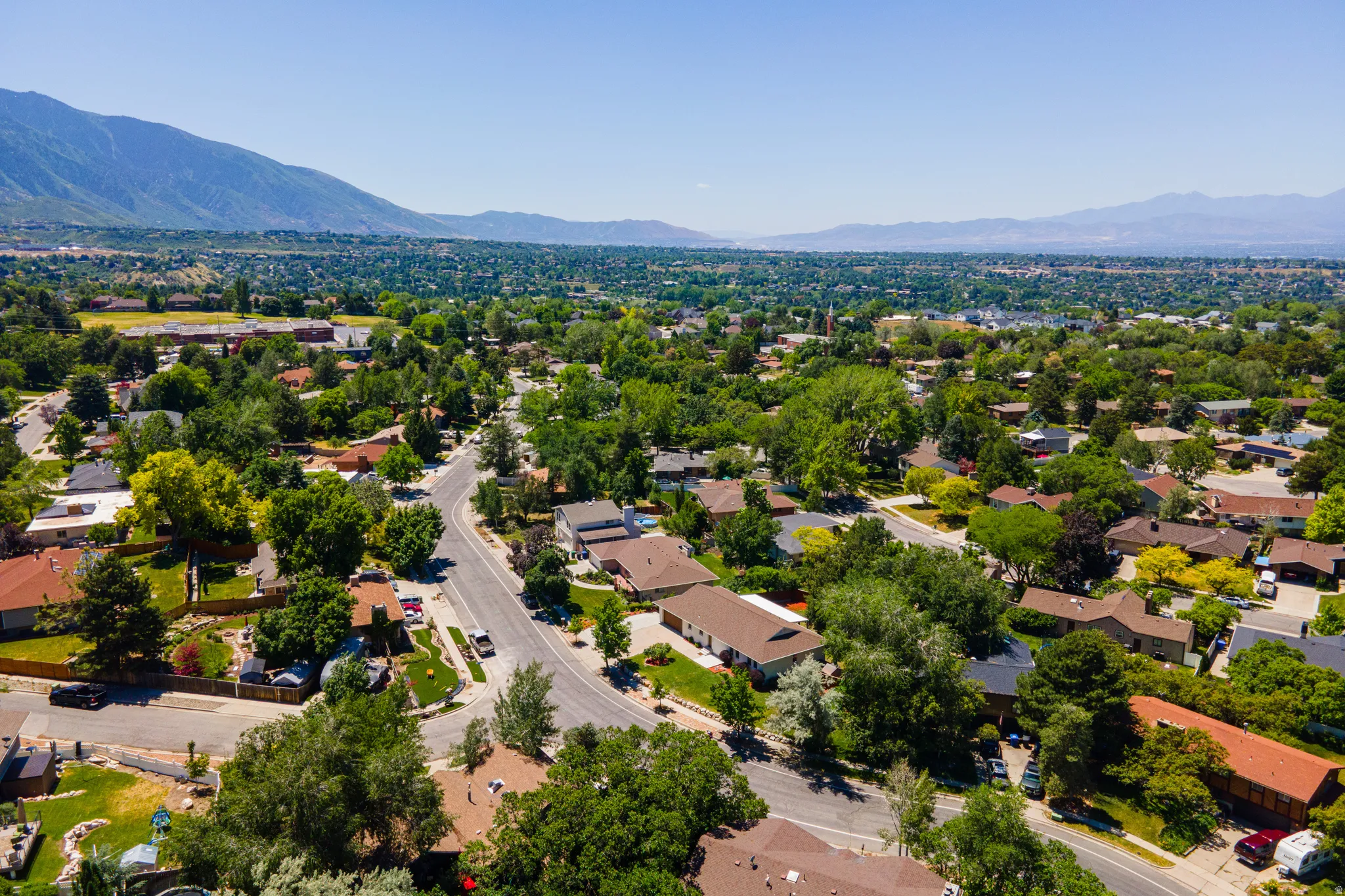 Expansive residential area featuring established homes, mature trees, paved streets, and mountainous terrain in the background