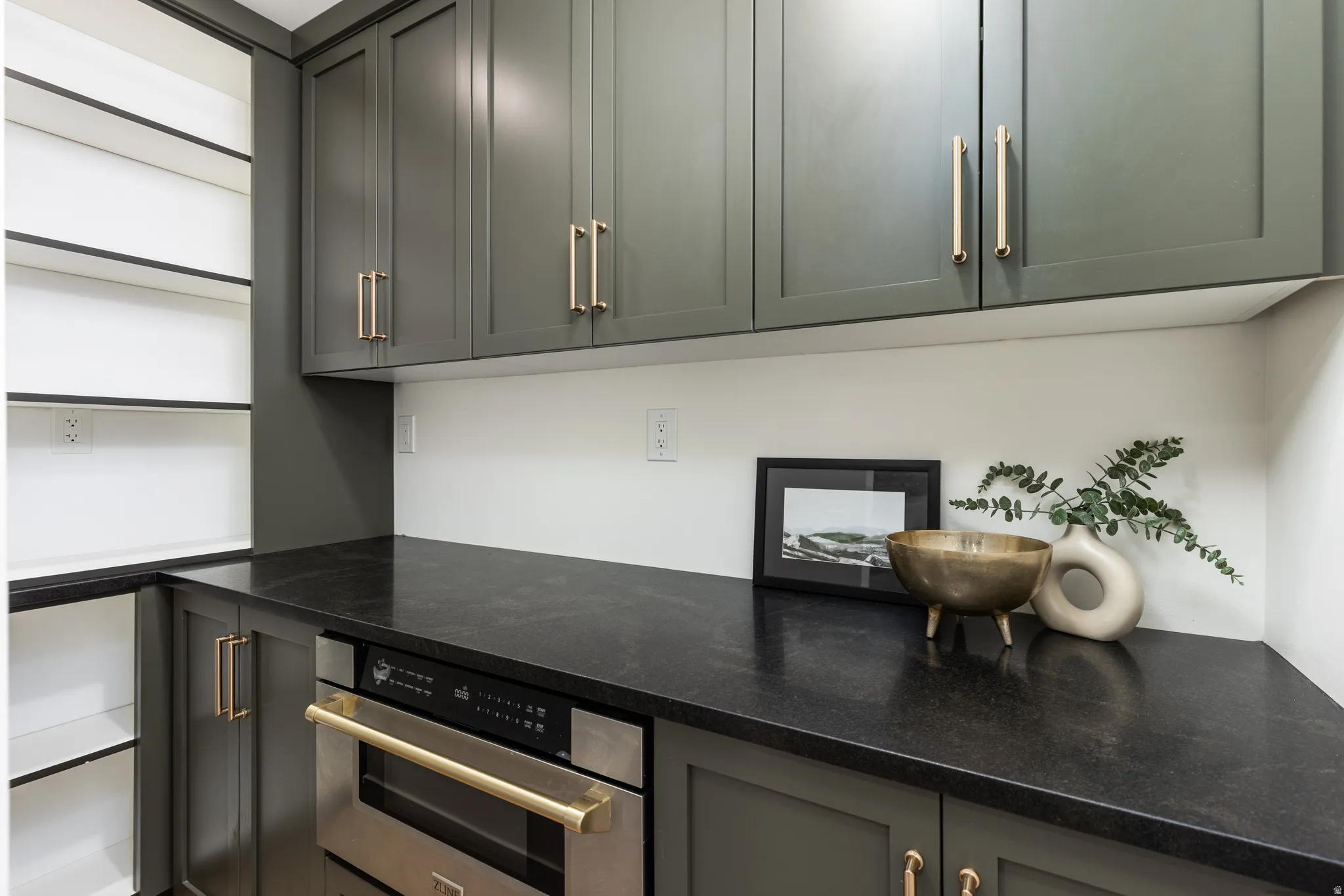 Built-in stainless steel microwave oven, dark countertops, white backsplash, and custom green cabinetry with gold-tone hardware