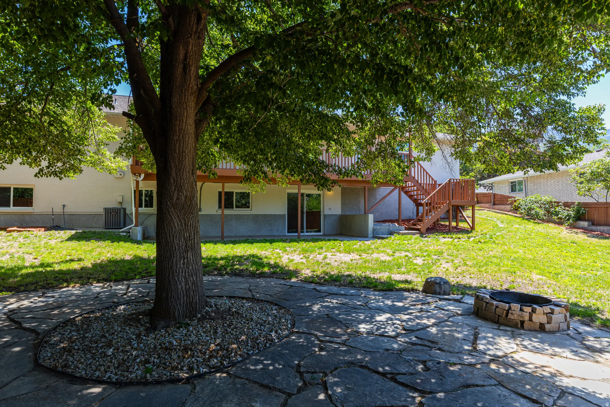 Expansive backyard featuring a natural stone patio, mature shade tree, and fire pit