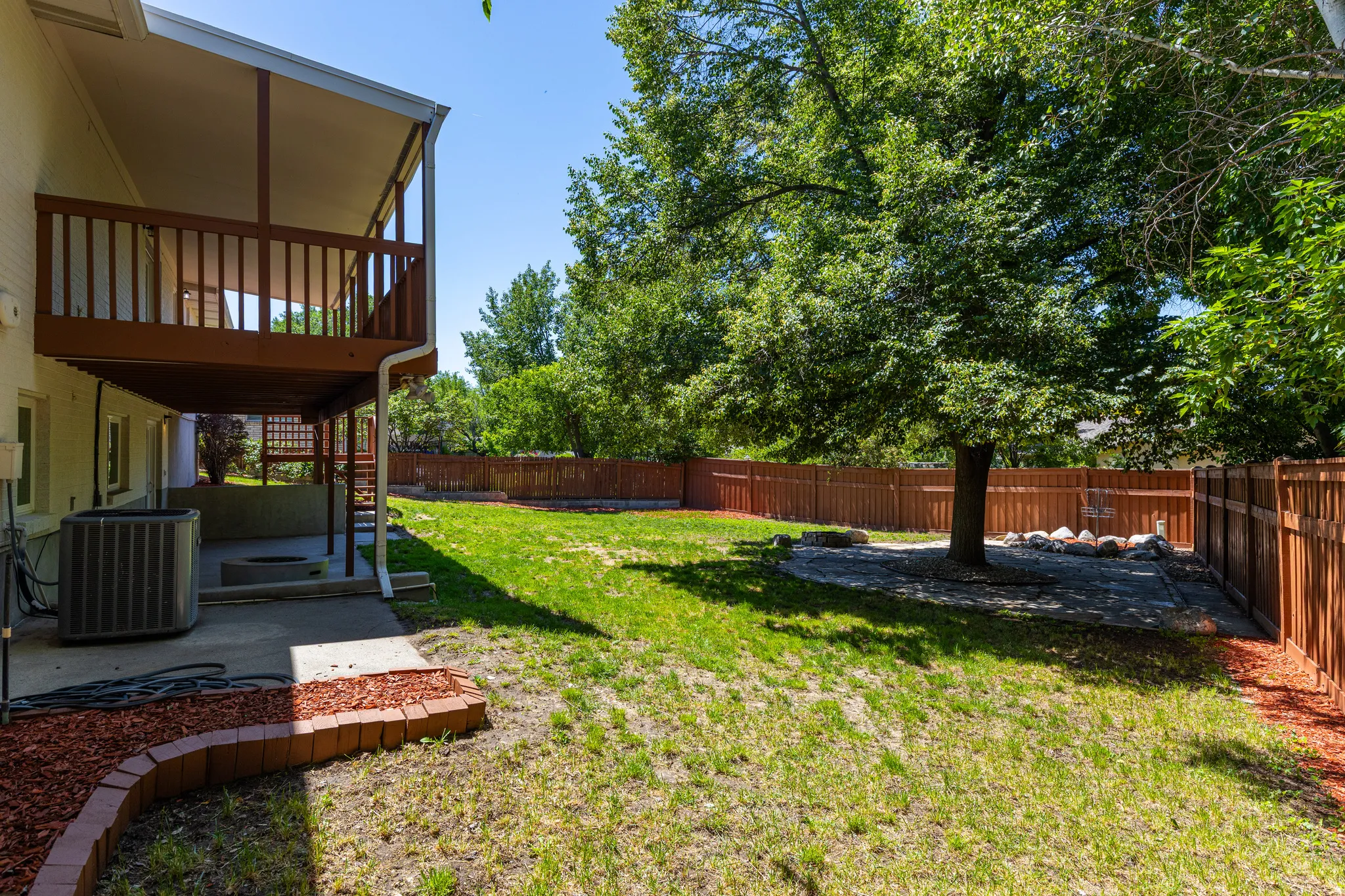 Expansive backyard featuring a manicured lawn, a large shade tree, and a full privacy fence