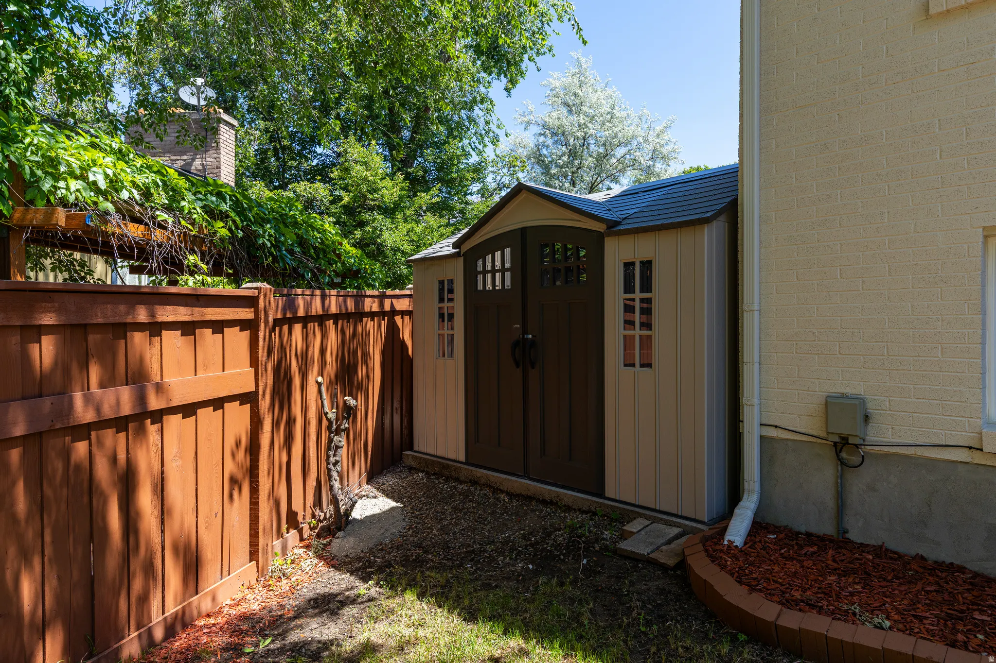 Outdoor storage shed featuring double doors with decorative windows and a peaked roof