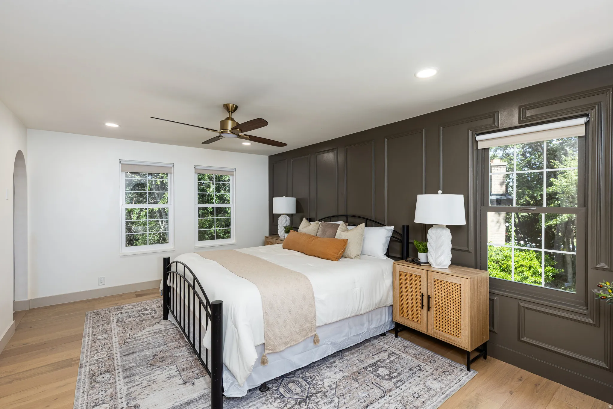 Hardwood-finish flooring complementing a paneled accent wall, recessed lighting, and a ceiling fan with integrated lighting