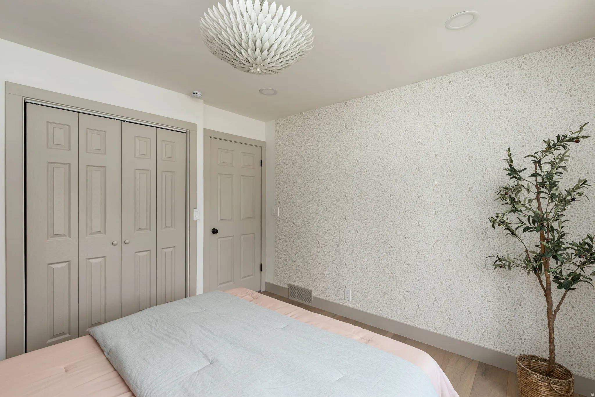 Bedroom featuring light wood-finish flooring, a contemporary ceiling light fixture, bi-fold closet doors, and textured wall finish