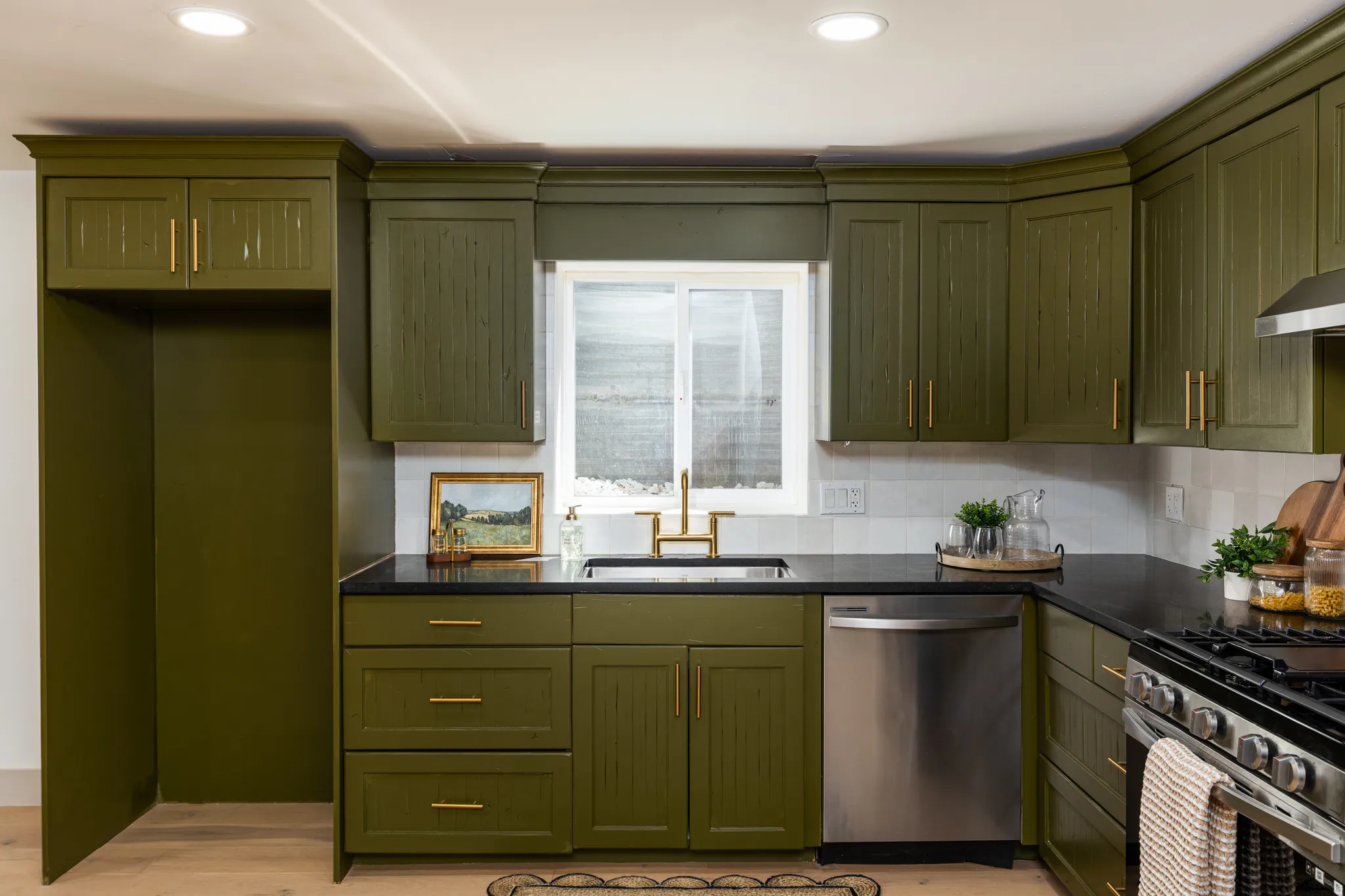 Kitchen featuring rich green cabinetry with gold-tone hardware, dark countertops, and a white subway tile backsplash