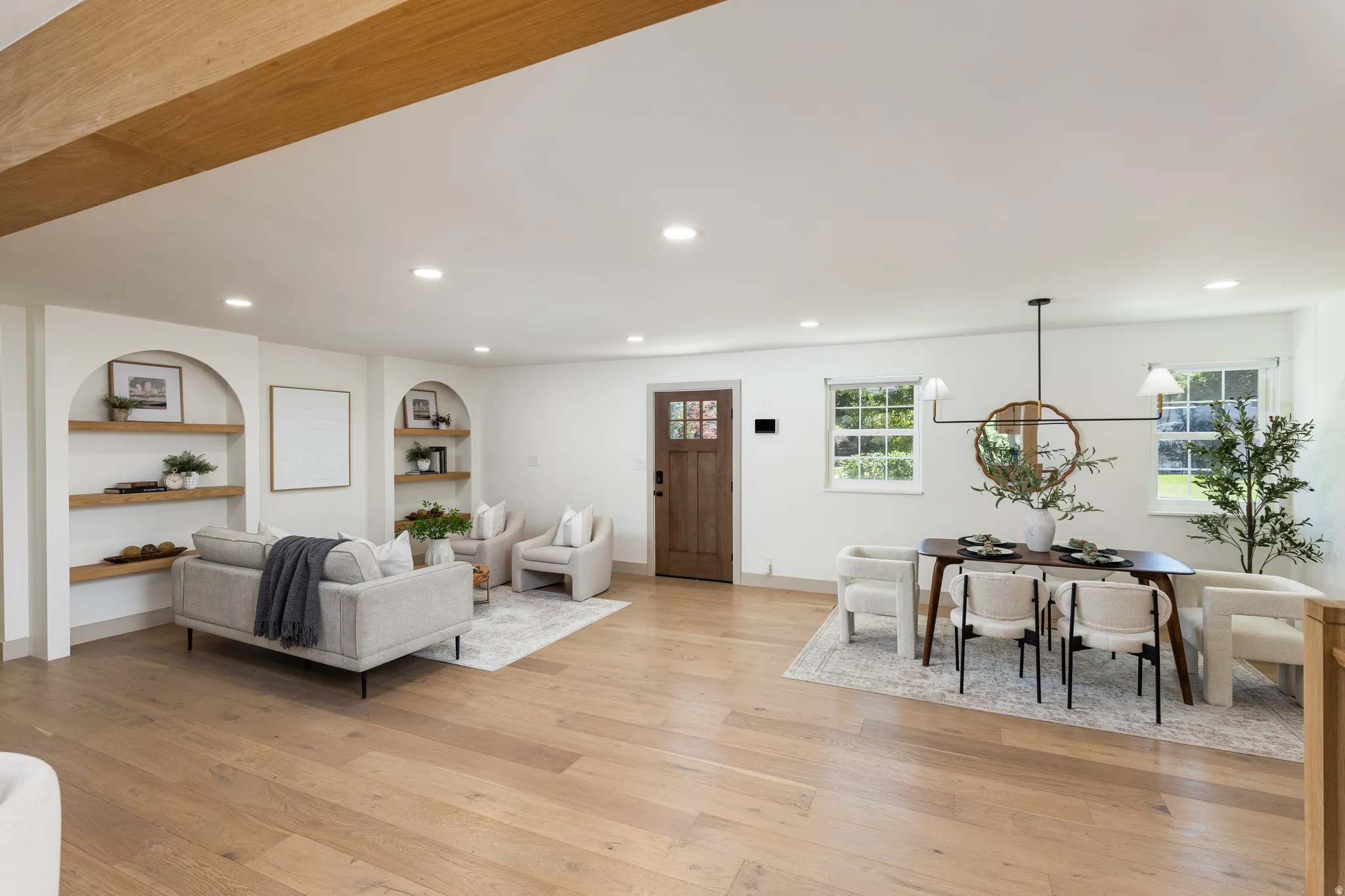 Expansive open-concept living space featuring light wood-finish flooring, recessed lighting, and exposed ceiling beams