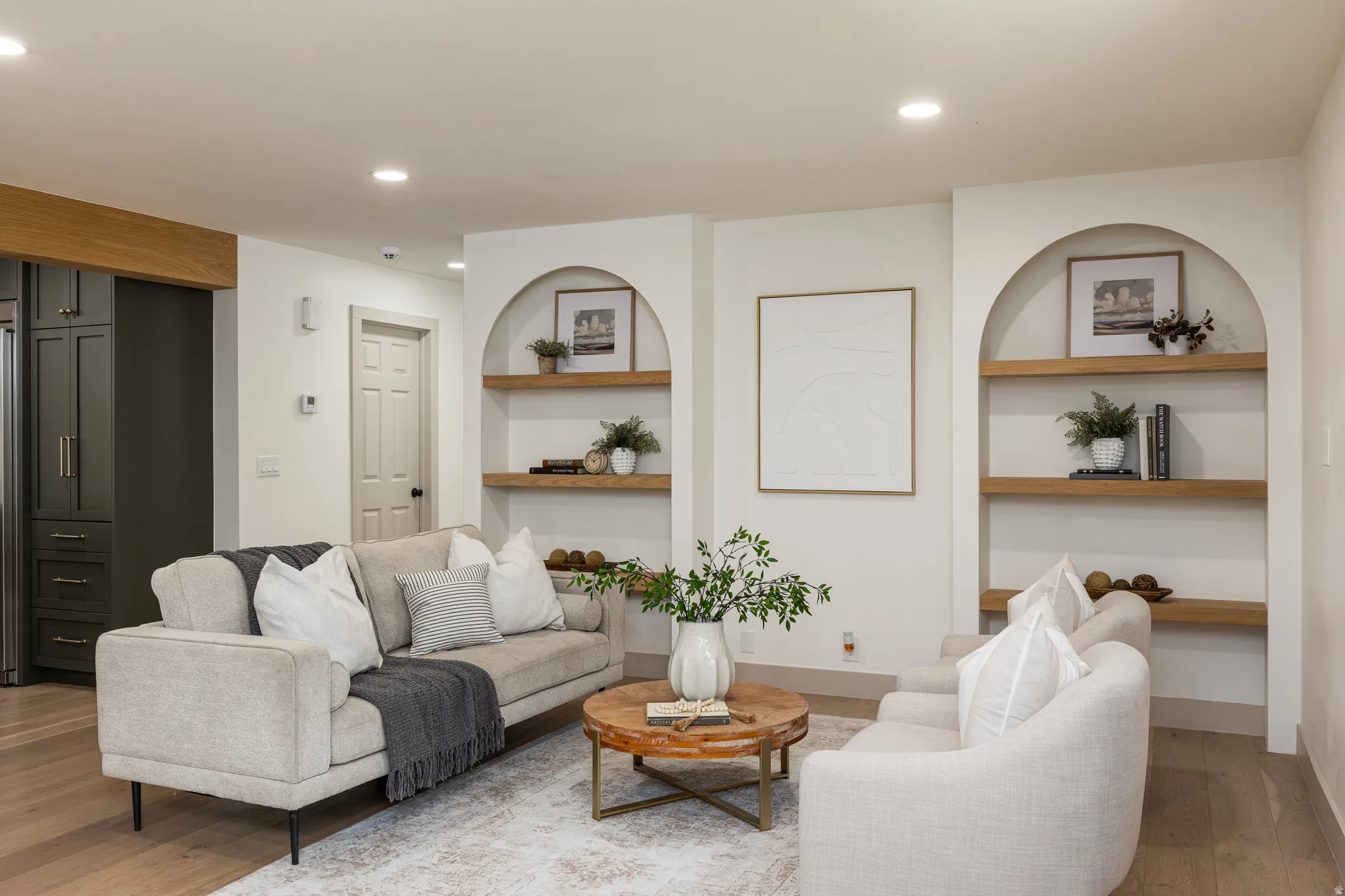 Living area featuring built-in arched alcoves with wood shelving, recessed lighting, and wood-finish flooring