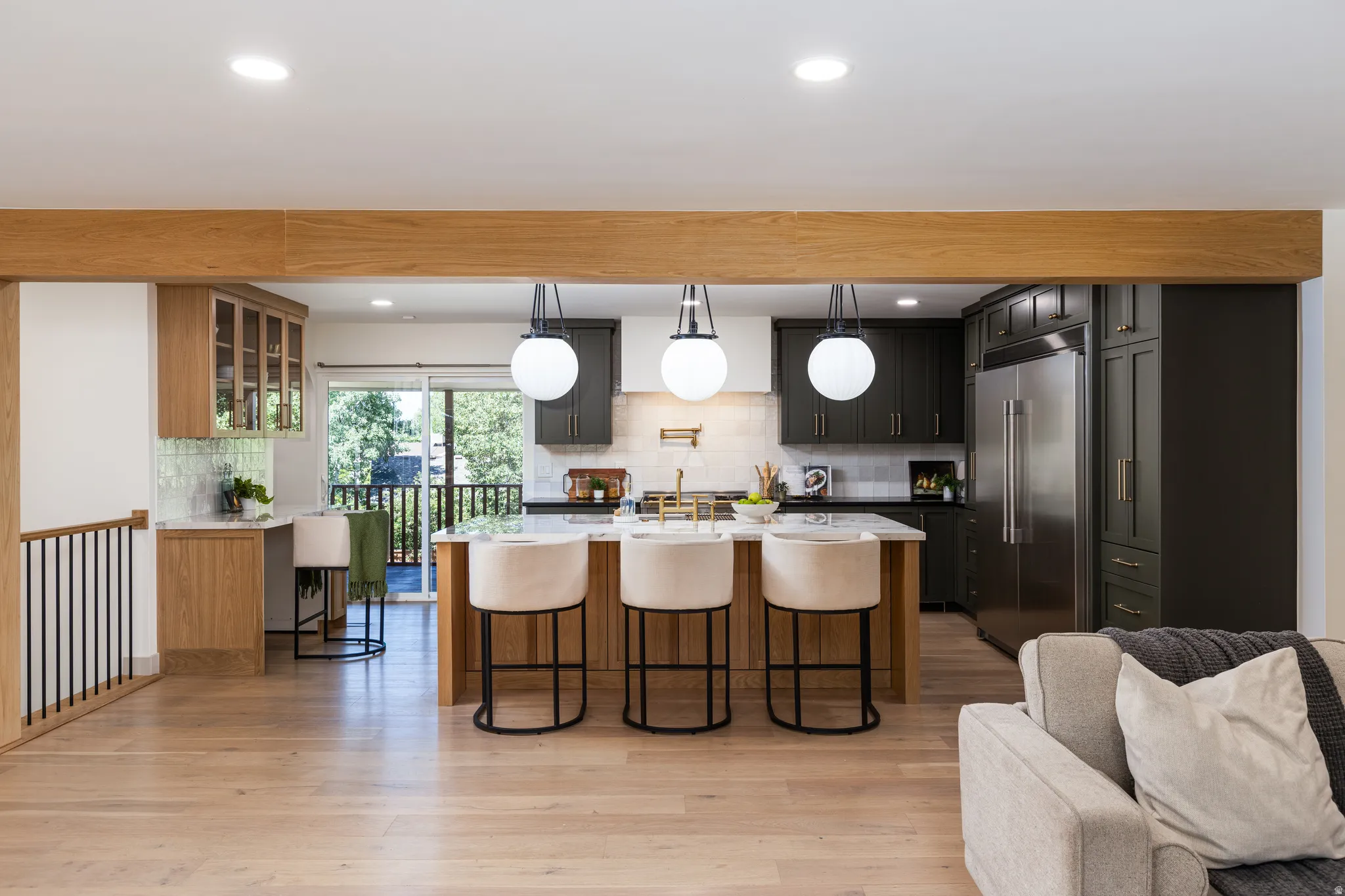 Open-concept kitchen featuring an island with seating, dark green cabinetry, stainless steel appliances, and a light wood-finish flooring