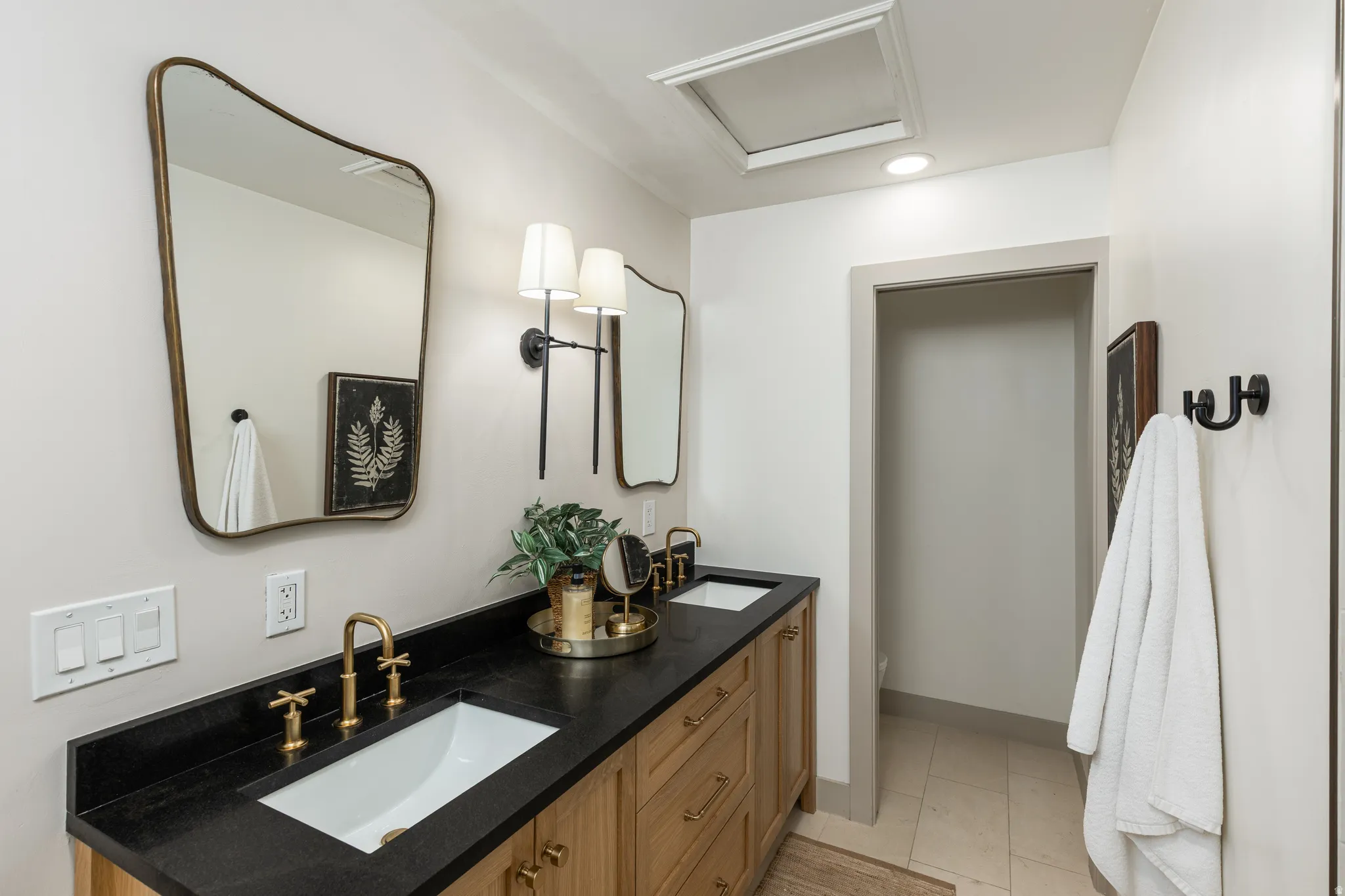 Bathroom featuring a double vanity with light wood cabinetry, dark countertops, and undermount sinks