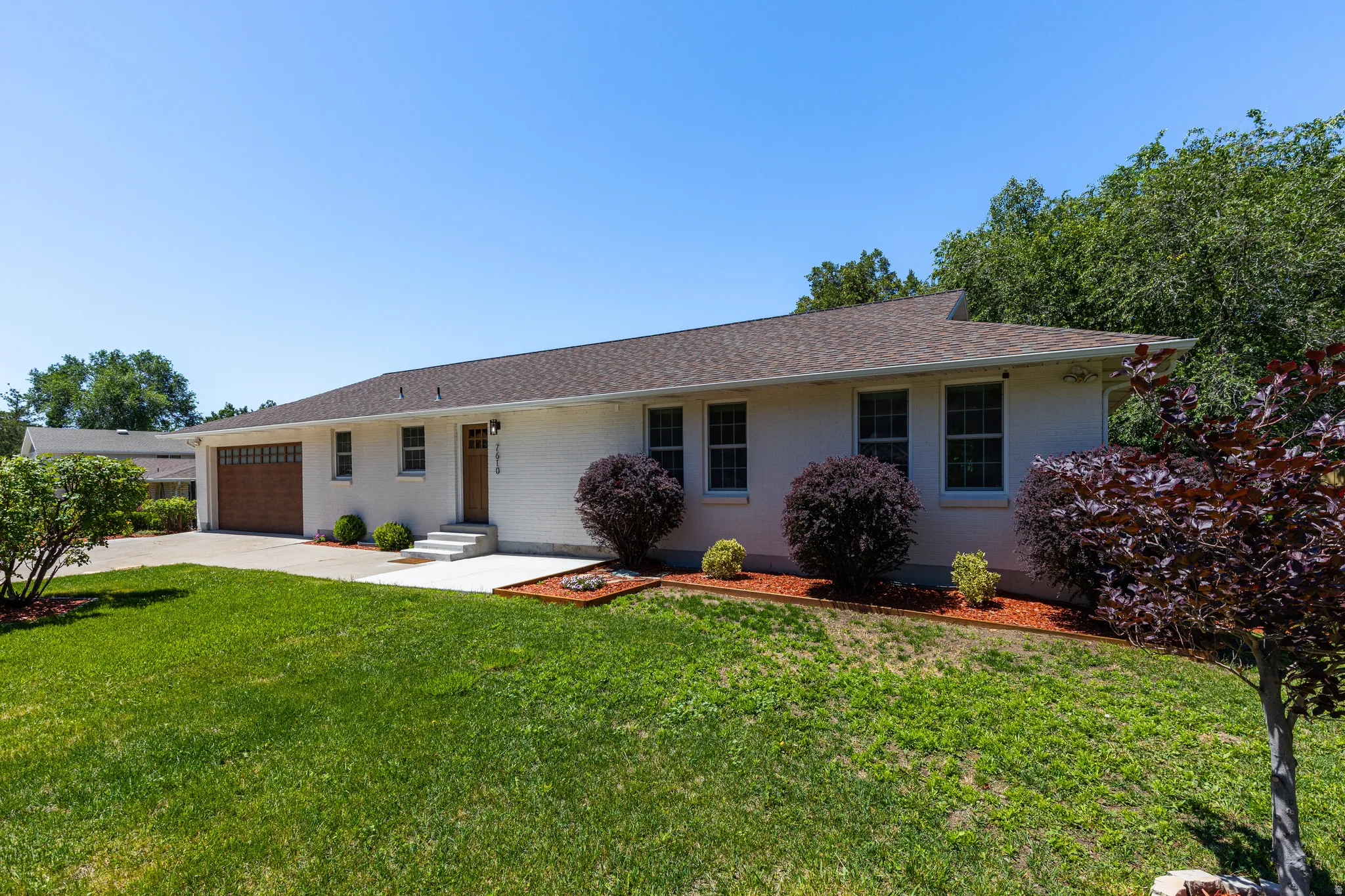 Ranch-style exterior with a white brick facade and a brown shingle roof