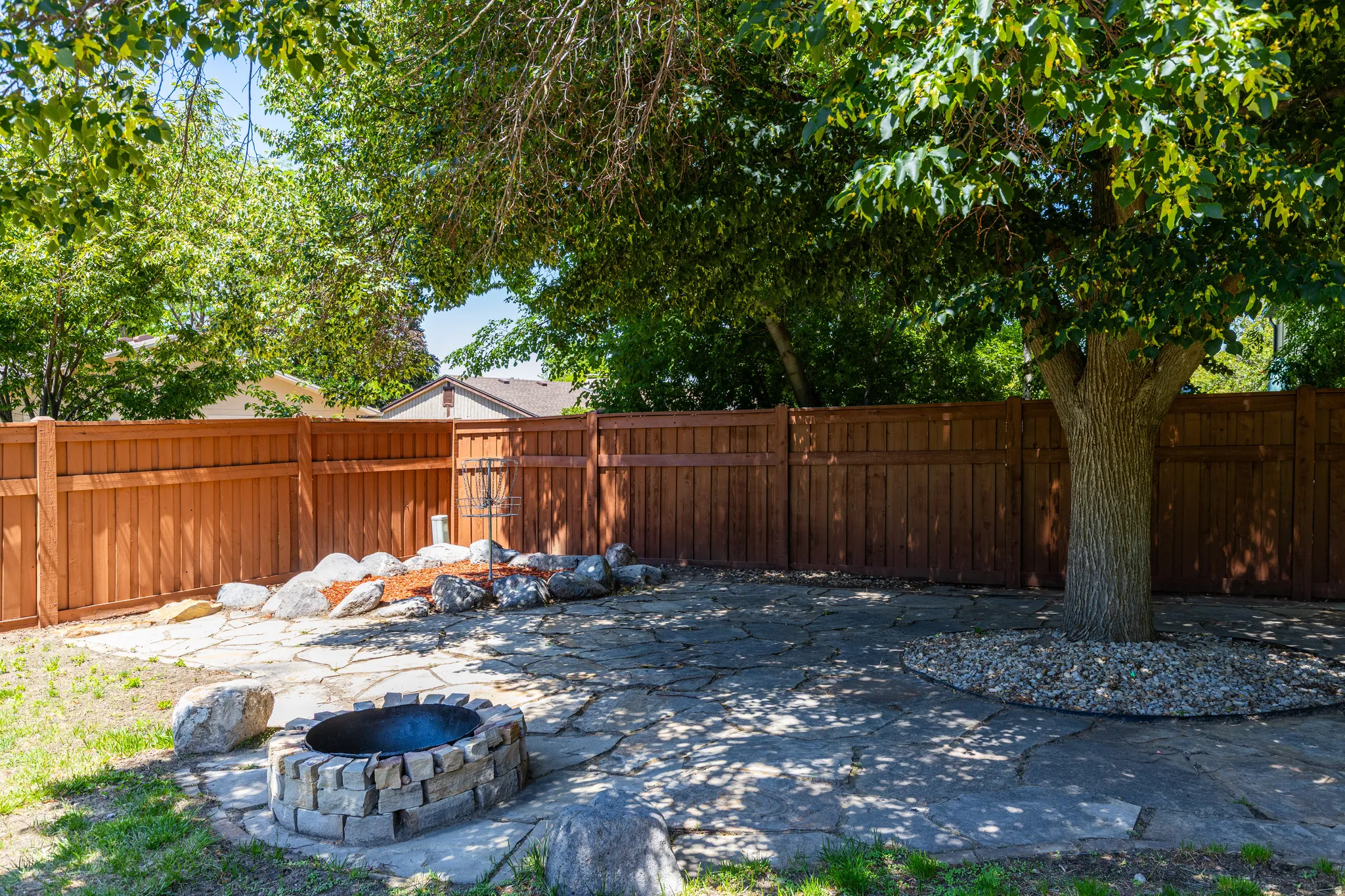 Backyard featuring a stone fire pit, extensive flagstone patio, and mature shade trees