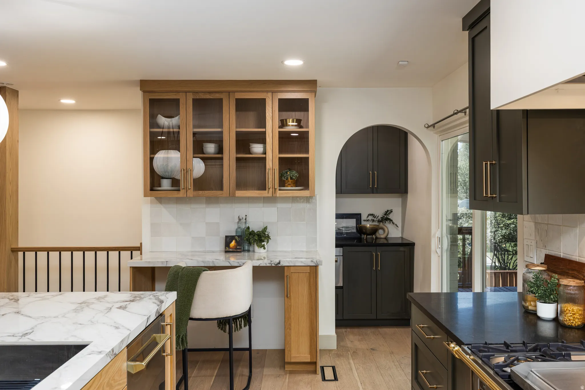 Gourmet kitchen featuring a built-in gas range, dark cabinetry with gold-tone hardware, wood-finish flooring, and white marble-look countertops