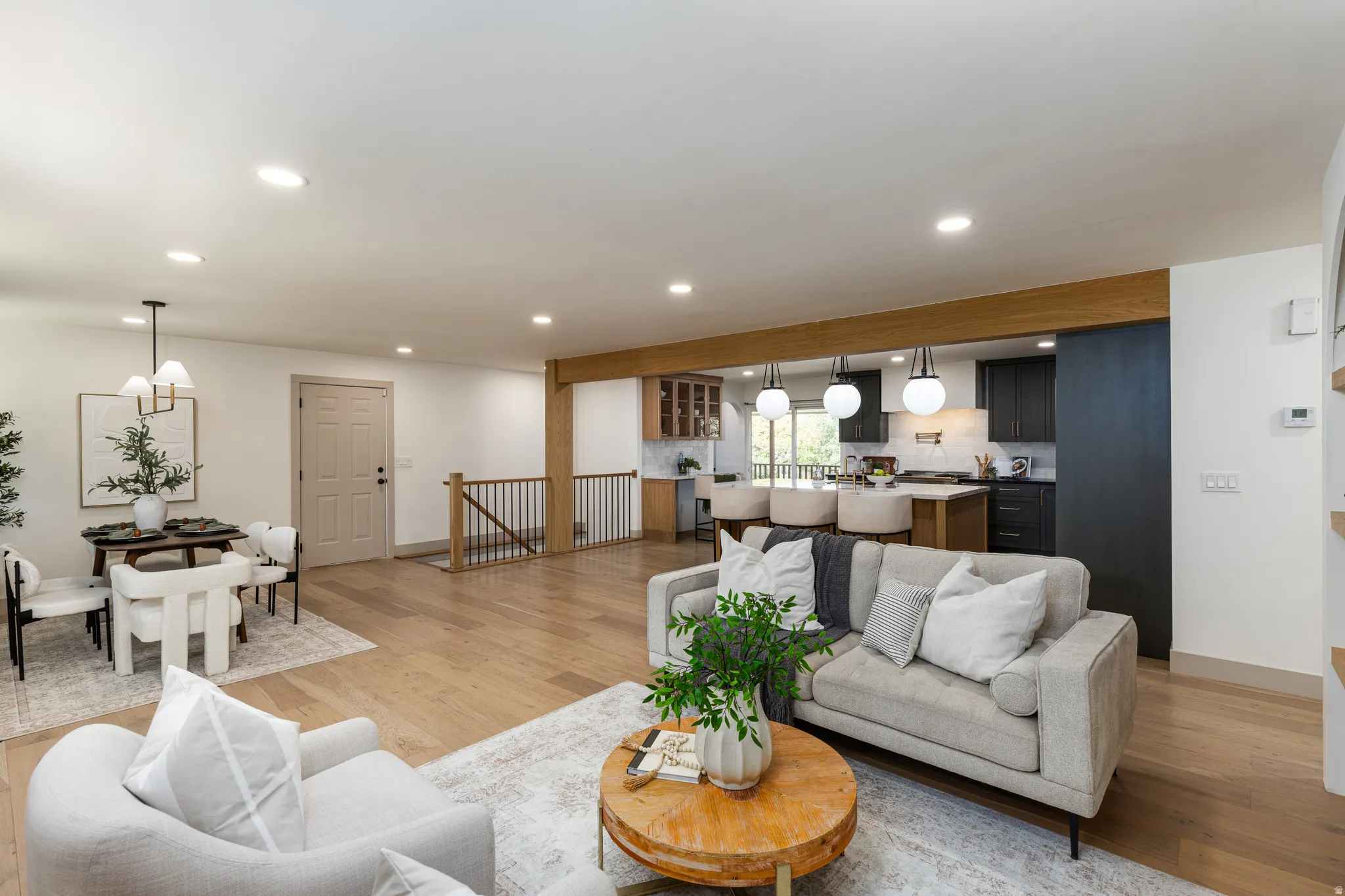 Expansive open-concept living area featuring light wood-finish flooring, recessed lighting, and a prominent wood beam detail