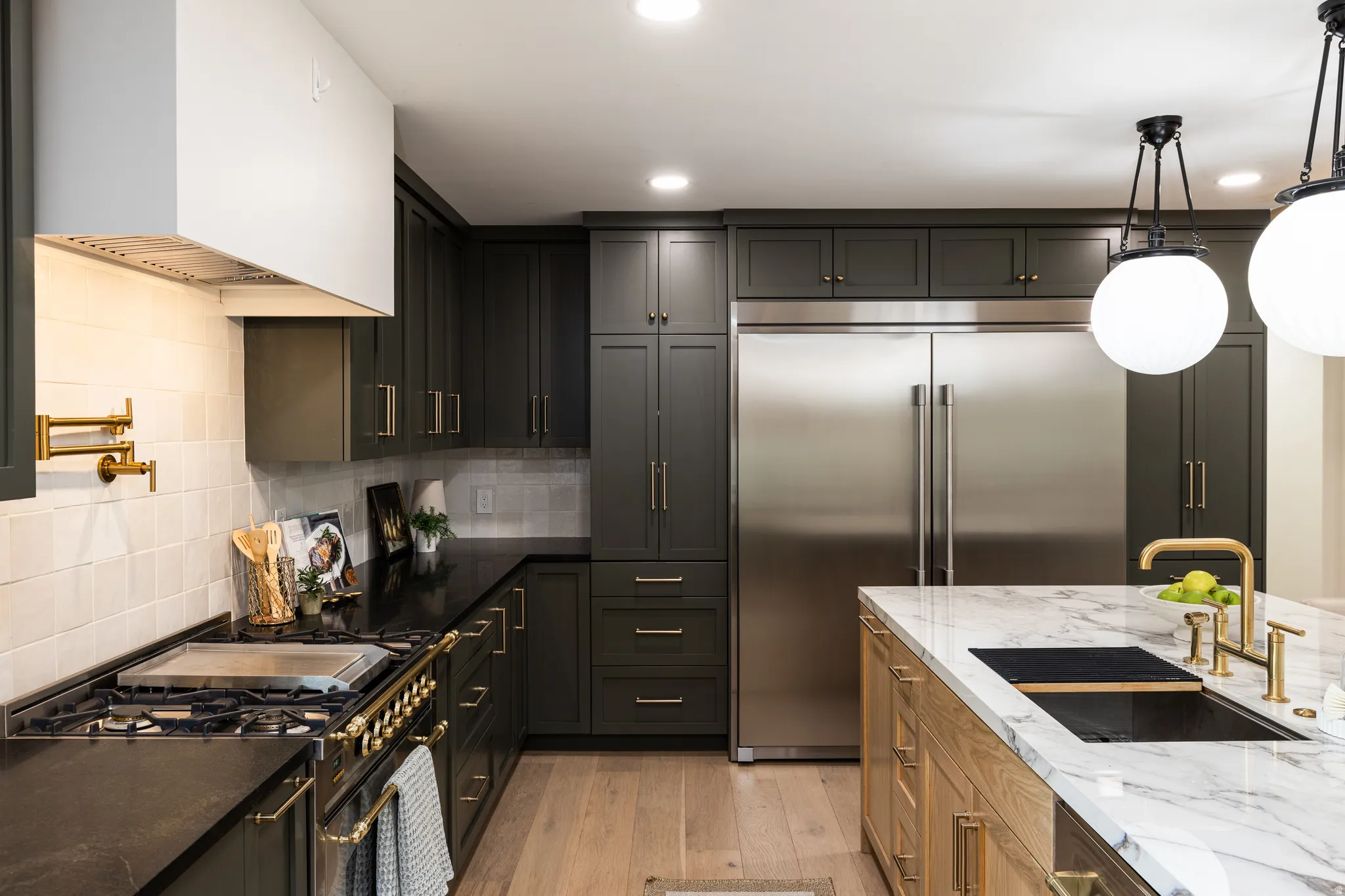 Gourmet kitchen featuring dark cabinetry, stainless steel appliances, black countertops, a pot filler, and a large central island with a white marble-patterned countertop and an undermount sink