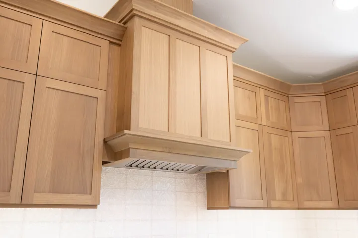 Custom wood cabinetry with crown molding, integrated range hood, and tile backsplash