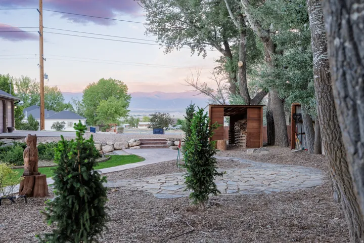 Stone pathway leading to a wood-sided storage structure, surrounded by mature trees and natural landscaping