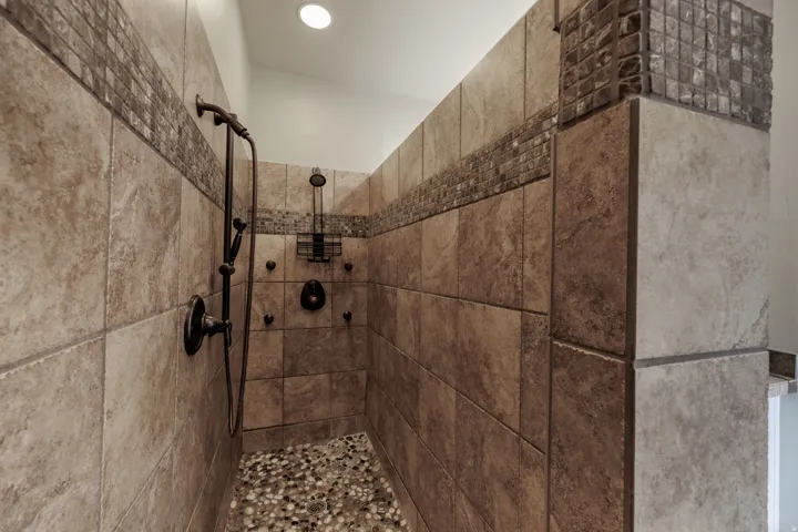 Walk-in shower featuring large format tile, pebble stone flooring, and a decorative mosaic accent band