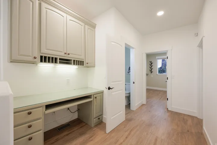 Built-in desk area featuring light-colored cabinetry, a glass countertop, and under-cabinet lighting