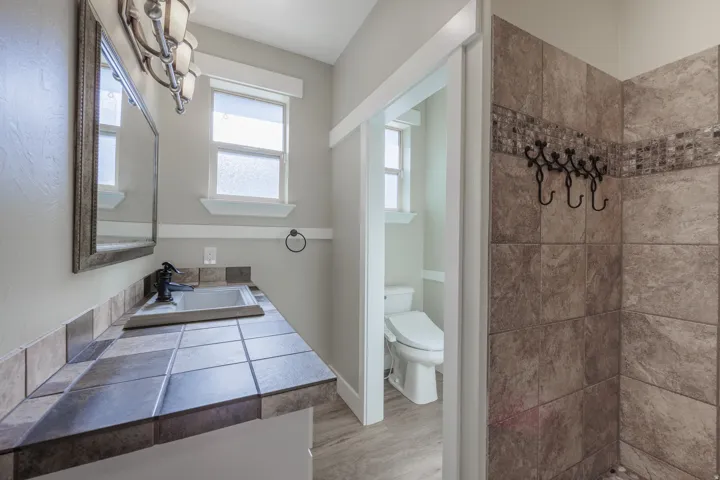 Bathroom with dual vanity featuring a tiled countertop, white cabinetry with dark hardware, and a framed mirror