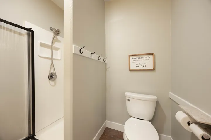 Basement bathroom, with Shower with glass enclosure and handheld showerhead, wall-mounted coat hooks, and toilet