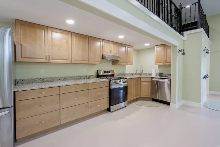 Open-concept kitchen featuring light wood cabinetry, stone countertops, stainless steel appliances, and recessed lighting