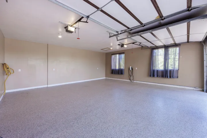 Spacious garage featuring a durable epoxy floor coating, two windows with curtain treatments, overhead lighting, and an electric vehicle charging station
