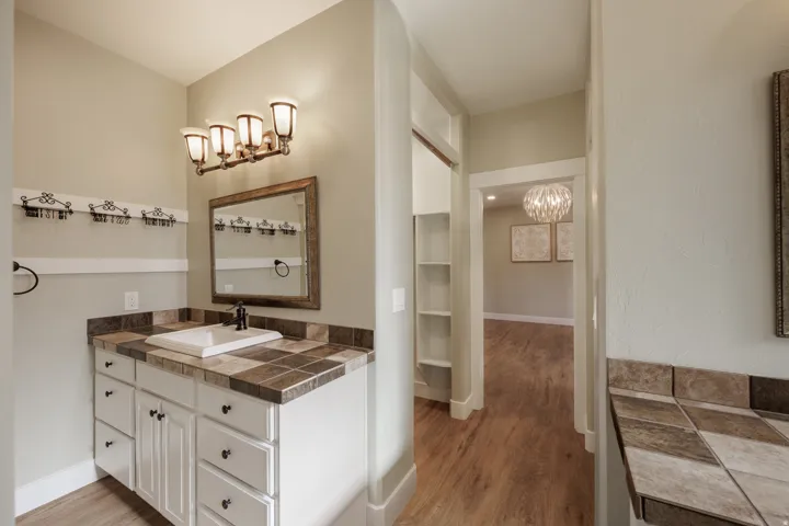 Bathroom with dual vanity featuring a tiled countertop, white cabinetry with dark hardware, and a framed mirror