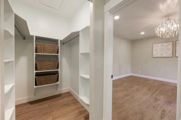 One of 2 Walk-in closets featuring built-in shelving, hanging rods, and wood-finish flooring