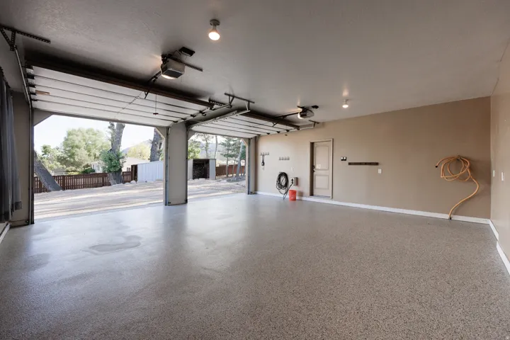 Spacious garage featuring a durable epoxy floor, dual overhead garage doors, overhead lighting, and interior access door