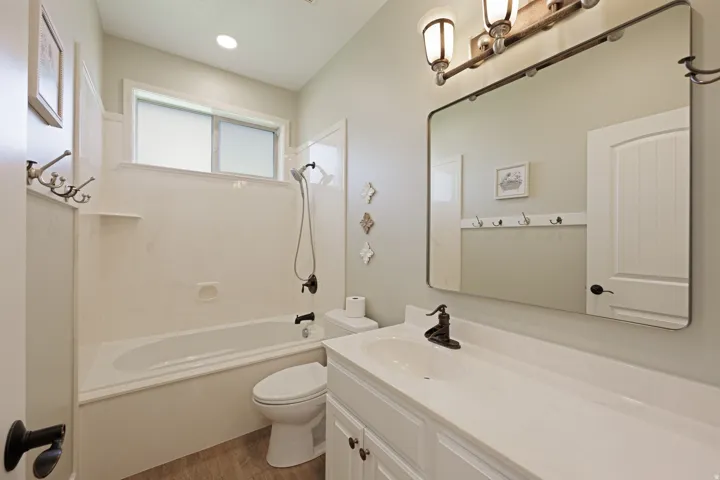 Bathroom featuring a single vanity with an integrated sink, a built-in jetted tub with a shower, a large wall mirror, and wood-finish flooring