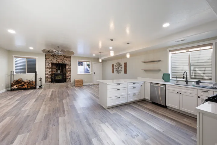Open-concept living area featuring wood-finish flooring, a stone-surround fireplace with a wood-burning stove, and recessed lighting