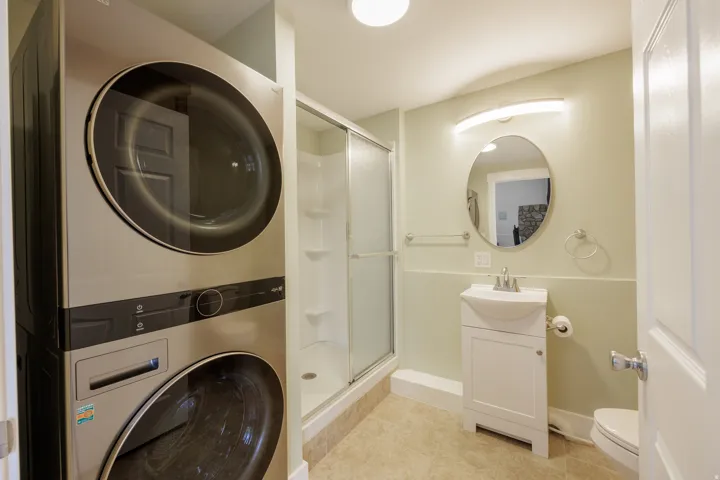 Bathroom featuring a stacked washer and dryer unit, a glass-enclosed shower, a white vanity with an integrated sink, an oval mirror, and neutral wall tones