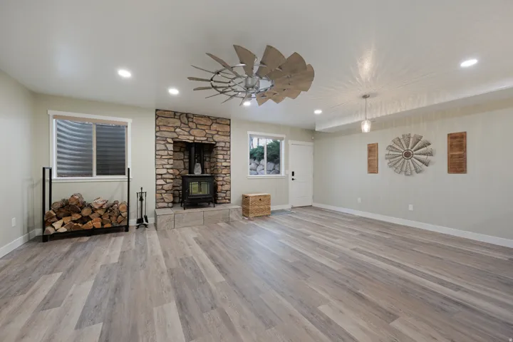 Spacious room featuring wood-finish flooring and a stone-clad fireplace with a wood-burning stove