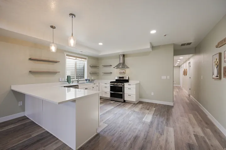 Modern kitchen featuring a large white island with a countertop extension, white cabinetry, stainless steel appliances, and wood-finish flooring