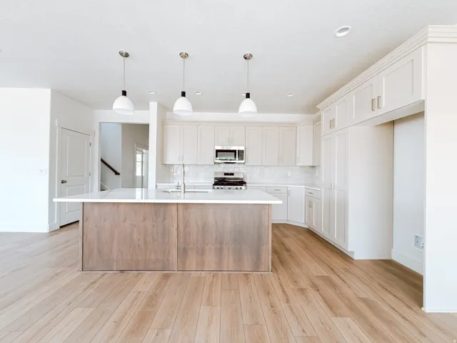 Modern kitchen featuring wood-finish flooring, a central island with a light-colored countertop, white shaker-style cabinetry, and stainless steel appliances
