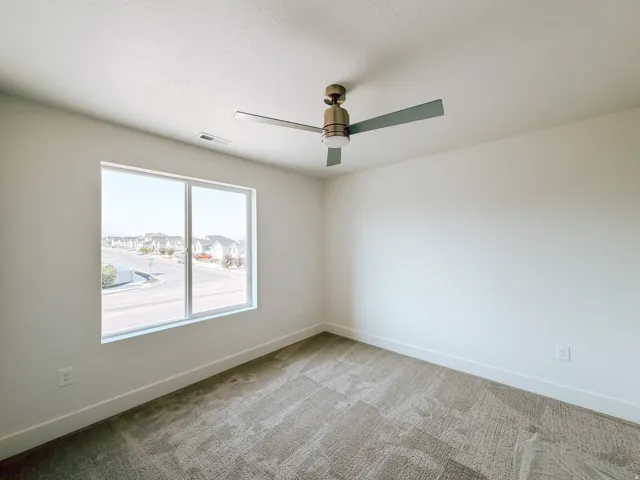 Neutral wall tones, modern ceiling fan, large window, and patterned carpet flooring