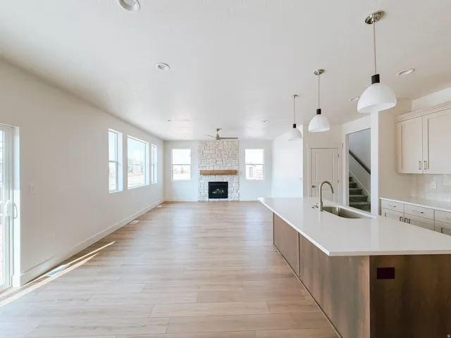 Open-concept living space featuring wood-finish flooring, a stone-surround fireplace with a wood mantle, and a kitchen island with a built-in sink and pendant lighting