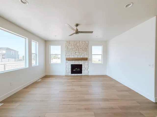 Spacious room featuring wood-finish flooring, a stone-clad fireplace with a wood mantel, multiple windows, and recessed lighting