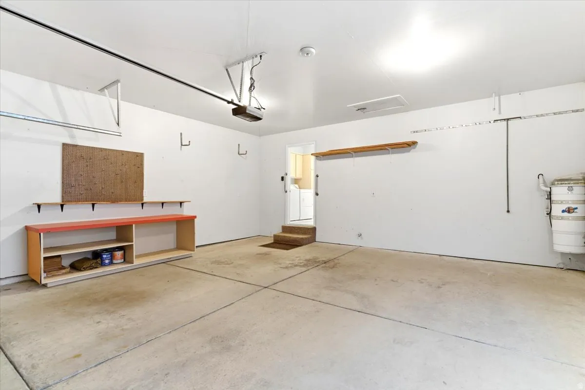 Spacious garage with concrete flooring, built-in shelving, a workbench, and a ceiling-mounted garage door opener