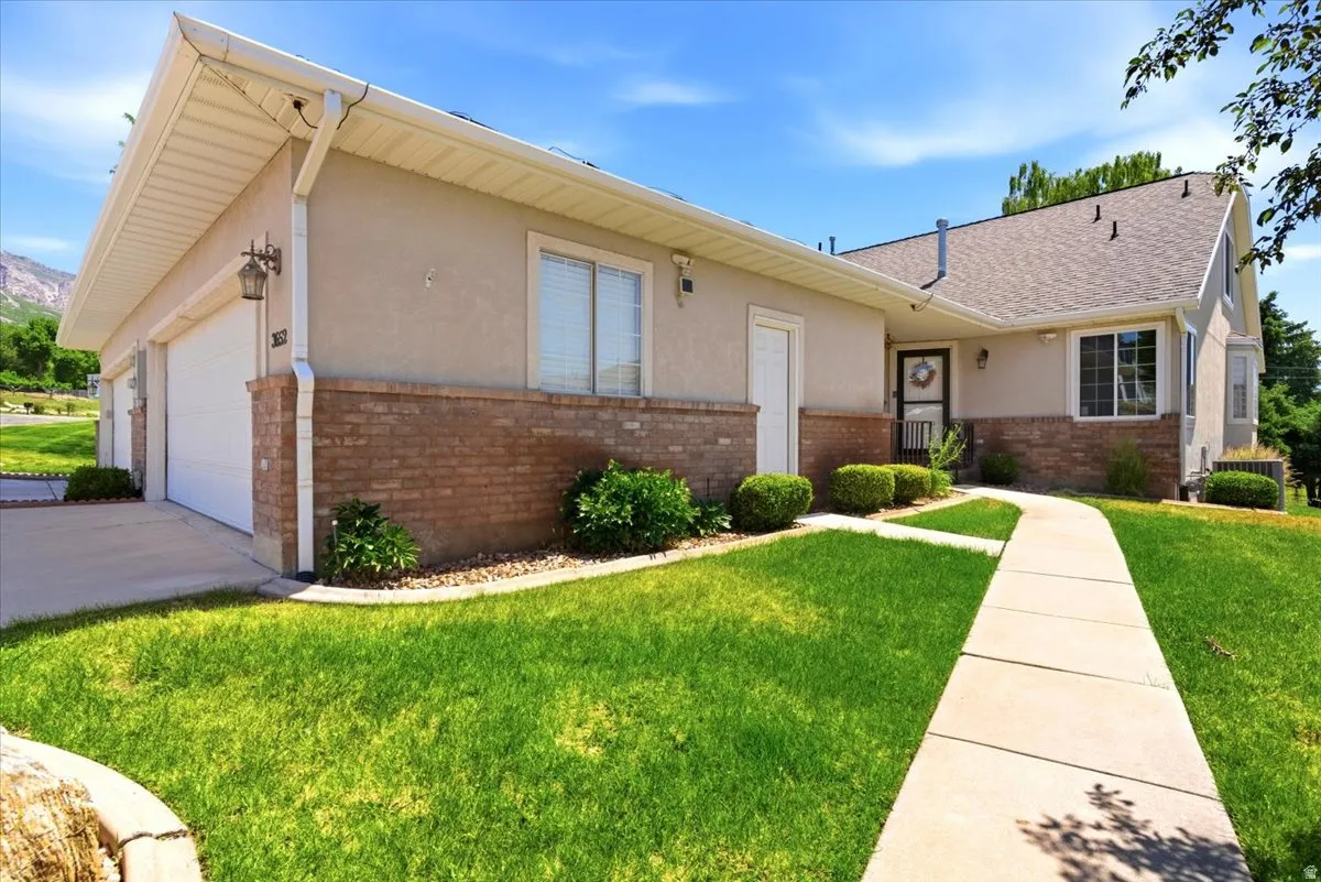 Exterior featuring stucco and brick finishes, a two-car garage, a concrete pathway, and landscaped shrubbery with a manicured lawn