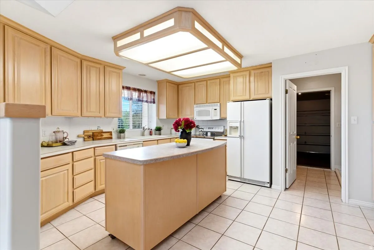 Kitchen featuring light wood cabinetry, white countertops, a moveable center island with a light-toned surface, tile flooring, and a pantry with built-in shelving